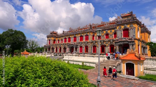 Majestic Kien Trung Palace featuring vibrant yellow walls, ornate ceramic mosaics, and striking red shutters against a cloudy blue sky.