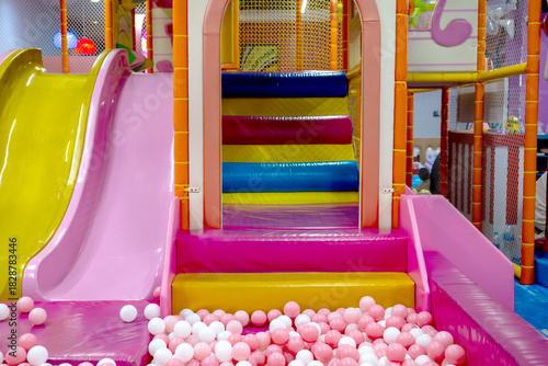 Colorful indoor playground with multicolored steps, pink and yellow slides, and a pink-white ball pit, creating a fun and safe play environment for children