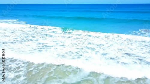 Crystal blue ocean waves gently lapping onto a sandy shore under a bright summer sky