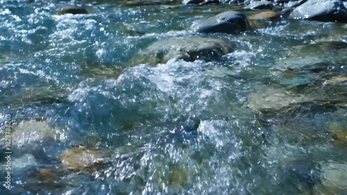 Crystal clear river water flowing over smooth stones and pebbles creating dynamic patterns and reflections of sunlight