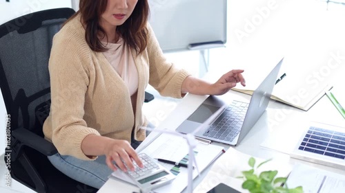 Asian adult woman calculating business finance laptop modern office sustainability renewable energy solutions project planning investment green economy