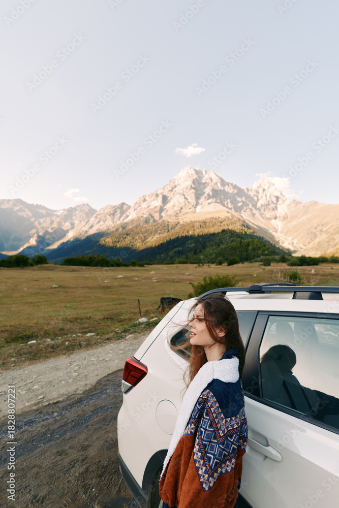 Fototapeta premium Woman and car parked by mountains on a travel roadtrip, landscape portrait in nature with autumn sweater, scenic meadow and sunlight creating calm adventure mood and freedom.