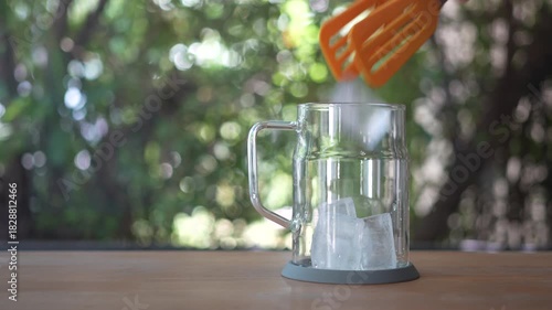 Hand using ice yellow tongs to put in the ice and prepare to make an iced beverage Summer drink. preparing water for brewing coffee, alcohol, and cocktails.