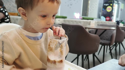 A cute little blonde baby sits in a cafe in a high chair and eats French fries, dessert, and drinks a cocktail. relaxes with her family. Happy childhood. Adorable little boy having breakfast at resort