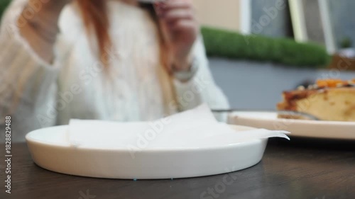 A girl in a cafe is eating dessert and drinking cappuccino, chatting on social media. A woman in casual clothes is sitting in the cafe, holding a smartphone in her hand and looking at it. 