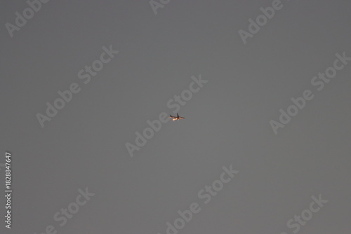 A plane flies in the sky before sunset with its exhaust out.