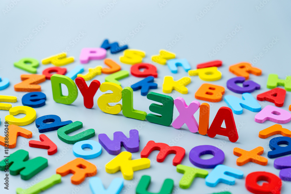 Naklejka premium The word DYSLEXIA is spelled out in colorful wooden letters scattered on a gray background. Learning difficulties, neurodiversity, educational challenges, reading struggles, and cognitive support.