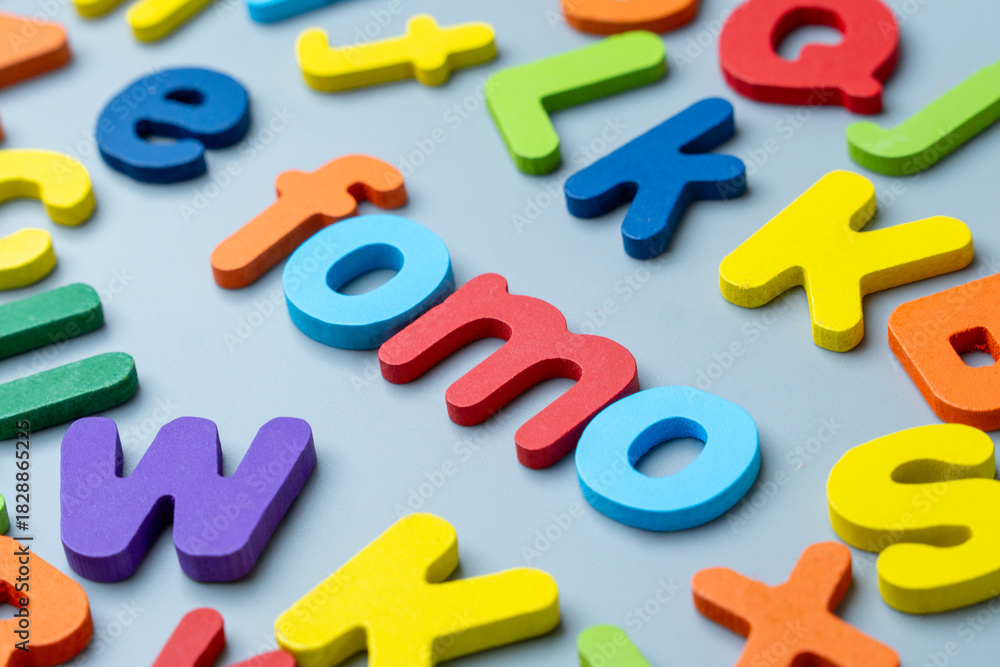 Naklejka premium Colorful wooden alphabet letters arranged to form the word FOMO. Fear of missing out, digital anxiety, social pressure concept.