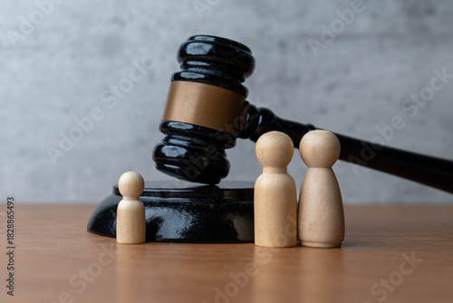 A wooden gavel stands next to three wooden peg dolls. Family law, guardianship, child custody, legal protection, and parental rights concept.