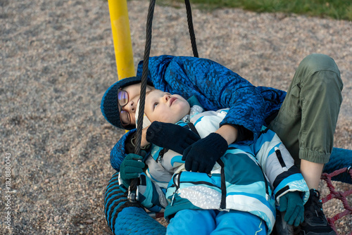 Cuadro en lienzo Two brothers lying together on nest swing looking up at sky at playground on autumn day close up portrait