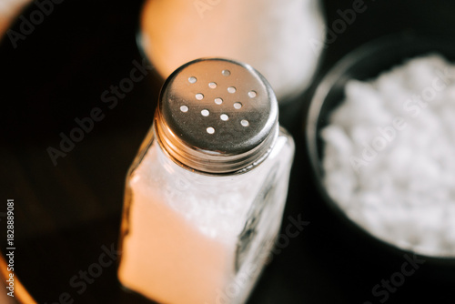 Salt shaker and bowl of salt on a wooden table with warm lighting