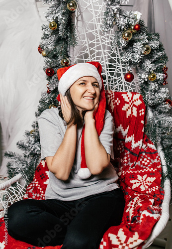 Smiling woman in festive hat sits on a decorative chair during holiday celebration at home