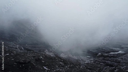 Calm drone orbit shot capturing the active crater of Mount Bromo, Java. White steam and smoke drift over the dark, rugged rock, creating a moody, dramatic volcanic scene.