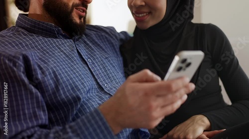Cheerful Muslim couple choosing luxurious items on phone, mobile shopping app