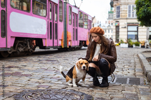 Woman petting a beagle dog on a cobblestone street with a pink tram