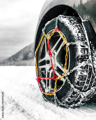 Winter car tire with snow chains mounted for safe driving in snowy conditions on a cold mountain road