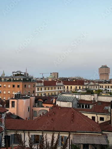 Panoramic Rooftop View of Milan's Historic Red Tile Roofs and Residential Buildings with the Velasca Tower and Duomo Spires Visible in the Skyline at Dusk