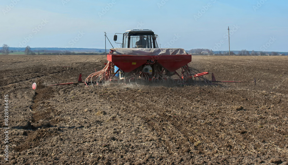 Fototapeta premium Farmer uses tractor to plant seeds in a freshly plowed field during early spring