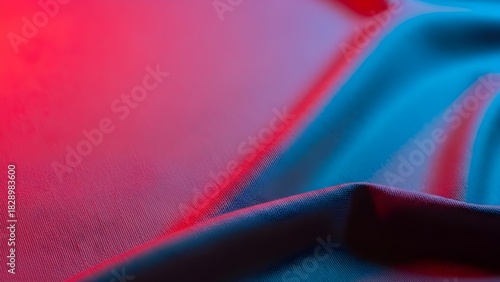 Illuminated fabric abstract: The smooth texture of a folded fabric is illuminated by a dynamic play of red and blue light. The colors intertwine and create a sense of depth and mystery.