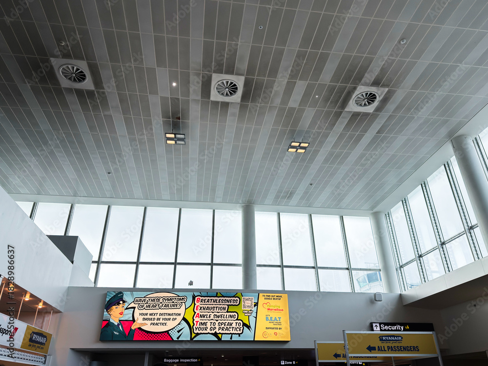 Obraz premium Bright Manchester airport terminal interior with large glass windows, banners, and security signage