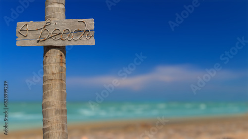 Signpost to the beach made from manila rope on old wooden board stick on coconut pole with blurred beach and blue sky background, Image for summer or travel theme with copy space and selective focus.