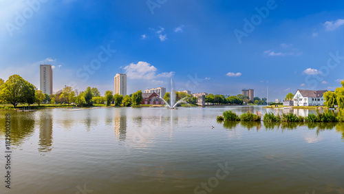 Panoramic view of the Watersportbaan in Ghent, Belgium, showcasing calm water, modern apartment buildings, and green surroundings under a clear blue sky