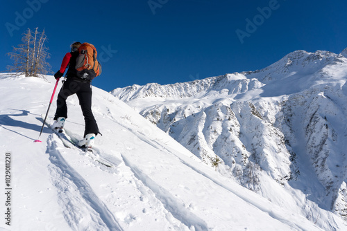 A woman pushing uphill in snowy terrain while skitouring in the French Alps.
