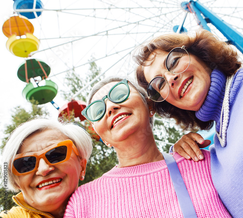Three elderly dates laugh and enjoy themselves while walking in front of a Ferris wheel at an amusement park.