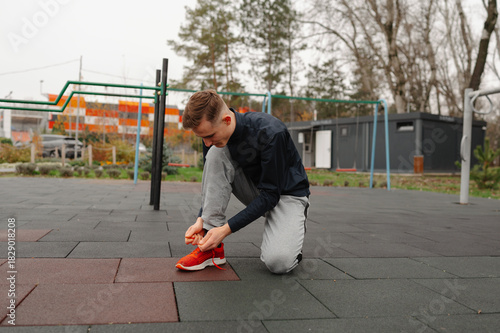 caucasian man tying shoelace outdoors park, kneeling on soft rubber mat, focused on footwear, preparing