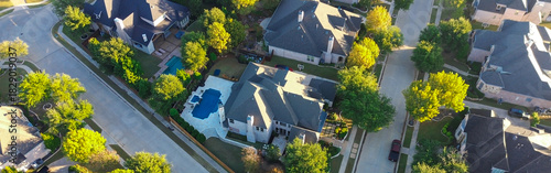 Panorama aerial densely packed homes in Lantana, Texas, arranged in grid with curved streets and cul-de-sacs, features varied rooflines, backyard pools, and tree-lined roads in green environment