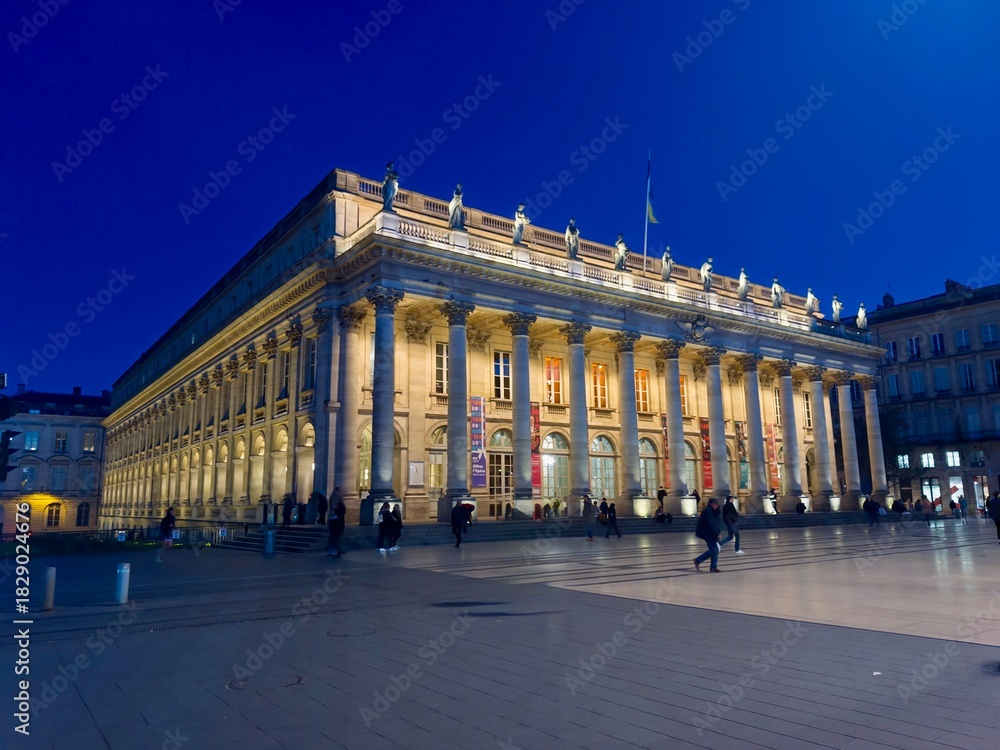 Obraz premium Magnificent Architectural Landmark Building Illuminated at Night with Grand Columns and Statuary in Bordeaux, France Captured with Vibrant Blue Sky