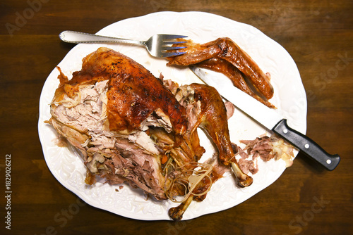 Partially carved Thanksgiving turkey on a white platter with knife and fork on a dark brown table.