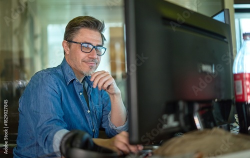Businessman working with computer in office. Business lifestyle - casual middle aged man sitting at desk in front of screen, smiling, happy.