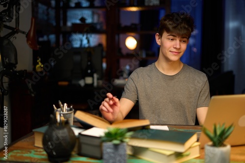 Teenage student learning at home with books and laptop computer. Online school and education, sitting at desk.