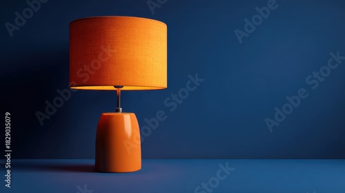 A bright orange lamp stands on a blue surface, showcasing its unique design and warm light. The simple yet striking color combination enhances the decor of the space.