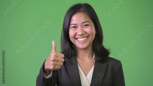 Woman in business attire giving thumbs up on green background