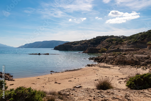 Fototapeta Naklejka Na Ścianę i Meble -  A tranquil sandy bay bordered by layered rock formations stretches out near Lopar on Rab Island, Croatia, capturing the unique geology and peaceful atmosphere of the sunny Kvarner region coast.
