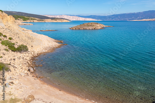 Fototapeta Naklejka Na Ścianę i Meble -  A secluded pebble beach meets the crystal clear turquoise water of the Adriatic Sea near Lopar. The sunny coastal landscape features rugged rocky terrain on the scenic Rab island in Croatia.