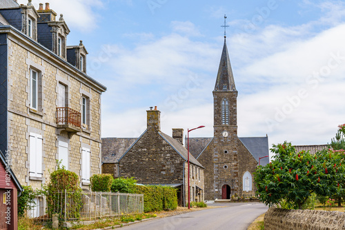 Fototapeta Naklejka Na Ścianę i Meble -  A small town with a church and a few houses in Brittany France. The houses are old and the church is tall. The sky is clear and the sun is shining