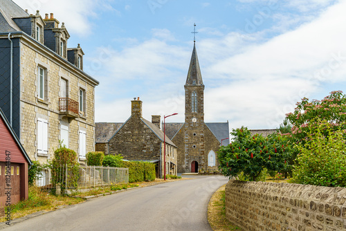 Fototapeta Naklejka Na Ścianę i Meble -  A small town with a church and a few houses in Brittany France. The houses are old and the church is tall. The sky is clear and the sun is shining
