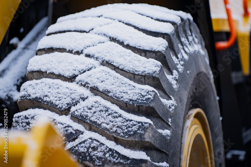 Detailed look at a thick winter coated construction vehicle tire displaying strong tread blocks and snow buildup commonly seen in cold industrial environments