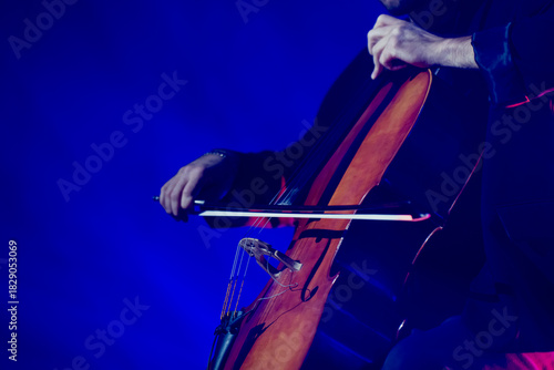 Close up scene of a cello player illuminated by intense blue light beams highlighting the instrument’s warm tones and dynamic motion of the bow