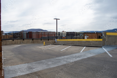 Empty concrete rooftop parking deck with a solitary light pole and a view of distant mountains and city buildings under a cloudy sky
