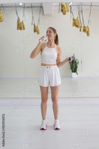 Smiling Woman Hydrating After Workout in a Bright Gym