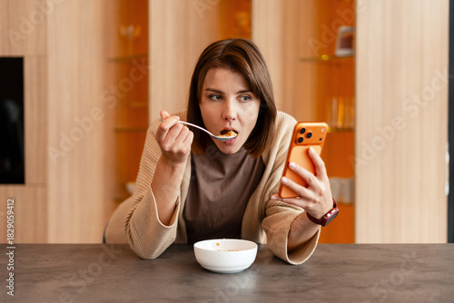 Canvastavla Young woman eating breakfast while using smartphone distracted