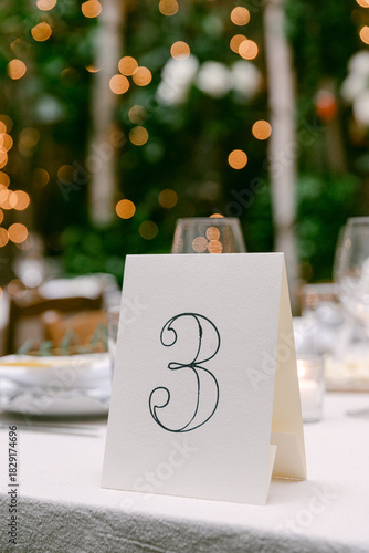 Elegant table number three set against a beautiful bokeh background at an outdoor event