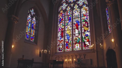Ornate stained glass windows casting vibrant light inside a historic gothic church, with flickering candles illuminating architectural details and creating a serene, spiritual atmosphere