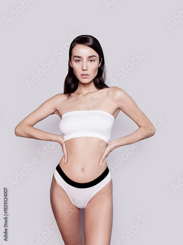 Gorgeous young woman with perfect body shape wearing lingerie underwear top and panties looking fresh happy and healthy posing on gray background