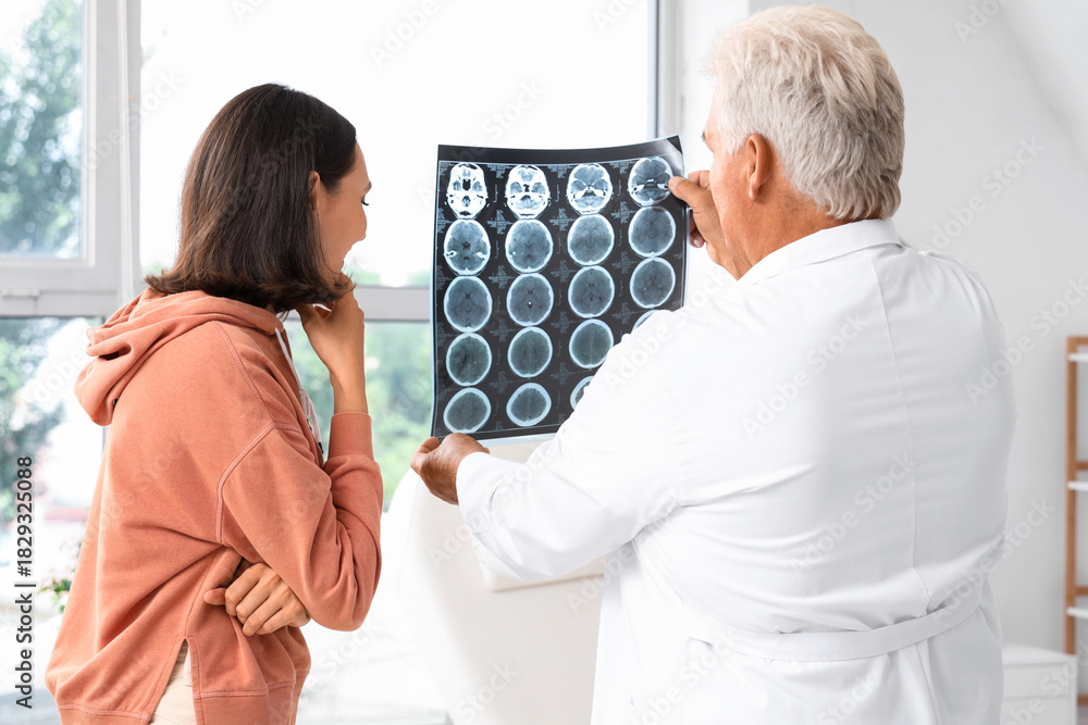 Fototapeta premium Senior doctor showing x-ray scan to young female patient in rehabilitation center
