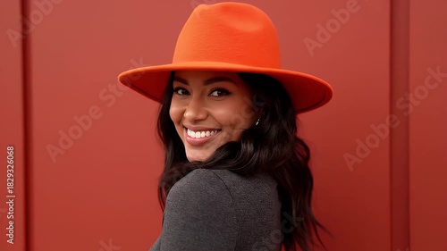 Portrait Of A Smiling Young Woman Wearing A Bright Orange Hat And Dark Turtleneck Against A Warm Red Background
